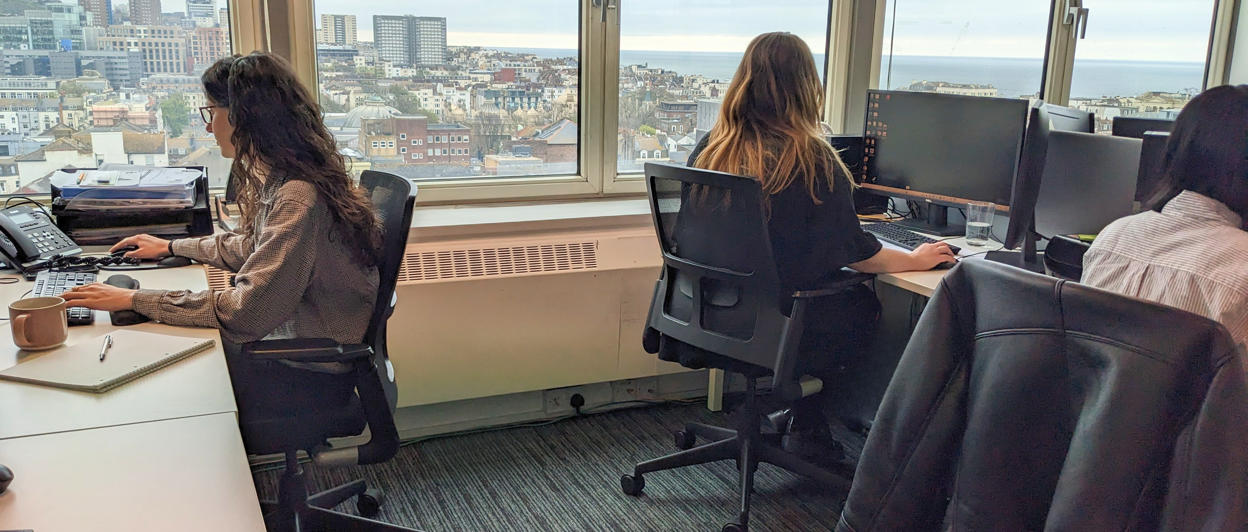 Three members of staff at the pre-employment training provider Tempus Training working at desks with a view over Brighton